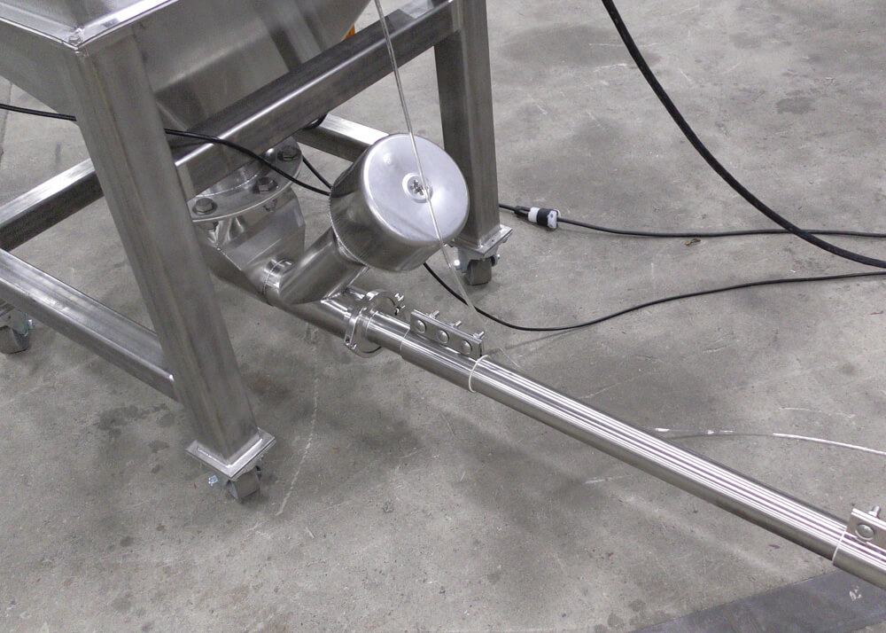 Stainless steel industrial hopper and attached pipe system with a cylindrical sensor component.