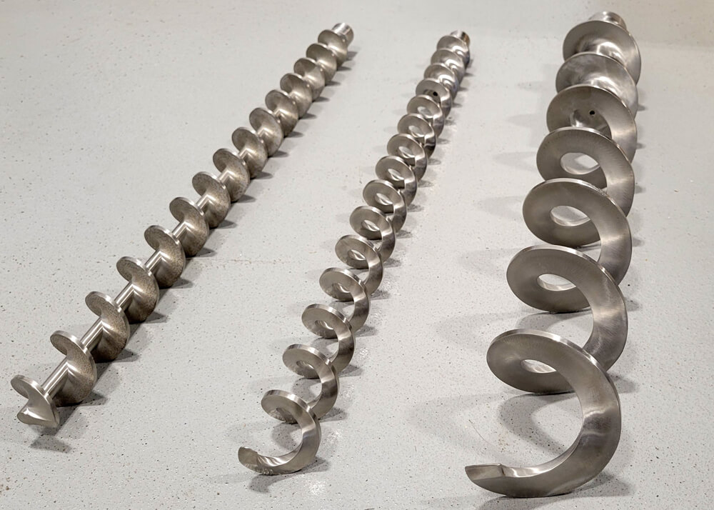 Three industrial metal augers of varying sizes laid out on a gray floor.