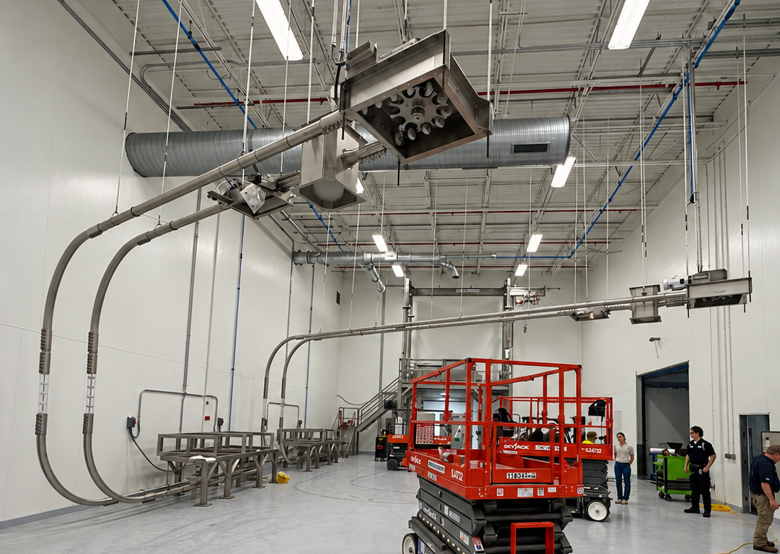 A ceiling-mounted industrial conveyor system with a red scissor lift below in a large warehouse facility.